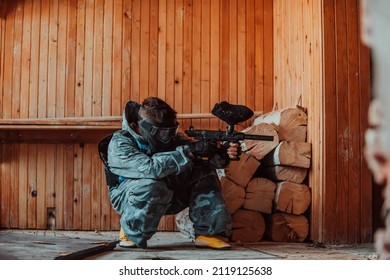 Photo of paintball player in goggle mask and camouflage aiming by a paintball gun. Selective focus. High-quality photo