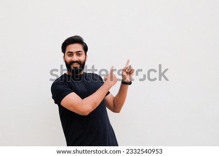 photo of Pakistani or Indian guy in casual wear, points finger to the side at empty space for your presentation