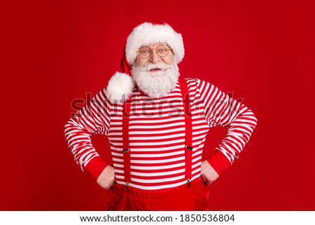 Photo of pensioner grandpa hands fists hips smiling wait newyear party event friend invitation wear santa costume suspenders spectacles striped shirt headwear isolated red color background
