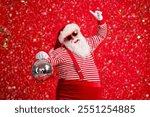 Photo of pensioner old man grey beard hold retro disco ball dance raise finger wear santa x-mas costume suspenders sunglass gloves striped shirt cap isolated red color background