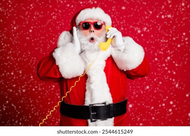 Photo of pensioner old man grey beard hold wired telephone talk collegue elves find out good news wear x-mas santa costume gloves coat belt sunglass cap isolated red color background - Powered by Shutterstock