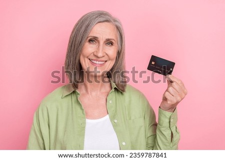 Photo of pensioner woman wearing khaki shirt holding black premium terms mastercard plastic advertise isolated on pink color background