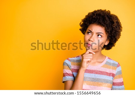 Photo of pensive concentrated focused girl contemplating empty space above her touching her chin isolated over yellow vivid color background