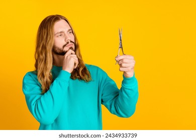 Photo of pensive man arm touch chin look hold scissors brainstorming empty space isolated on yellow color background