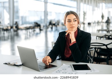 Photo of a pensive thoughtful elegant caucasian business woman, executive, recruitment, product manager, sits in a business center, working in a laptop, tired looking away, thinking, dreaming - Shutterstock ID 2268941839