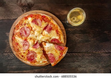 A photo of a pepperoni pizza with a slice cut off, with a glass of white wine, shot from above on a dark rustic texture with a place for text - Powered by Shutterstock