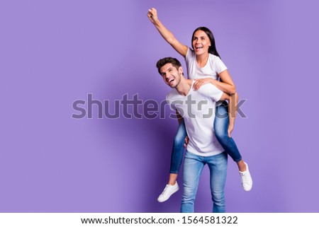 Photo of piggyback pretty cute couple in jeans denim white t-shirt with man carrying girl her directing him forward smiling toothily isolated pastel color background violet