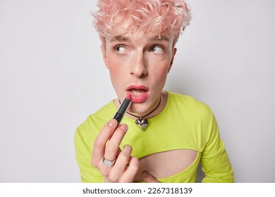 Photo of pink haired gay applies lipstick wears makeup wears feminine clothes prepares for date has women appearance isolated on white background. Non conforming queer man poses with cosmetic product - Powered by Shutterstock