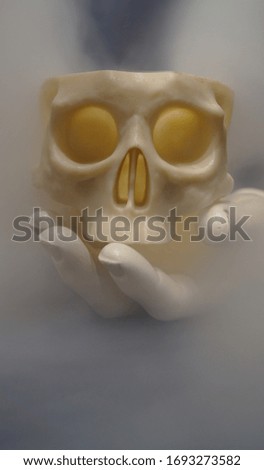 Photo of a plastic toy skull on a mannequin's hand against a background of smoke.