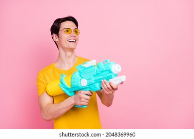 Photo Of Playful Funny Young Guy Dressed Yellow T-shirt Arm Shooting Water Gun Empty Space Smiling Isolated Pink Color Background