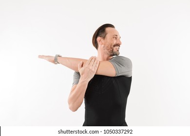 Photo of pleased sportsman 30s wearing smartwatch and t-shirt smiling and stretching arms while warming up isolated over white background