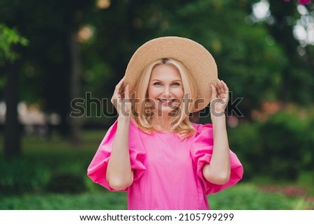 Photo portait smiling senior woman wearing hat pink clothes walking in green city park in spring