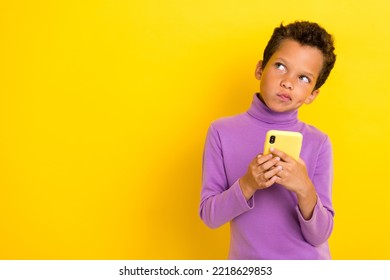 Photo portrait of adorable little boy hold telephone look skeptical copyspace wear trendy violet outfit isolated on yellow color background