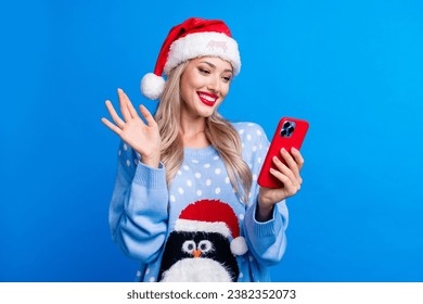 Photo portrait of attractive blonde woman hold device wave hand dressed penguin sweater x-mas hat isolated on blue color background - Powered by Shutterstock