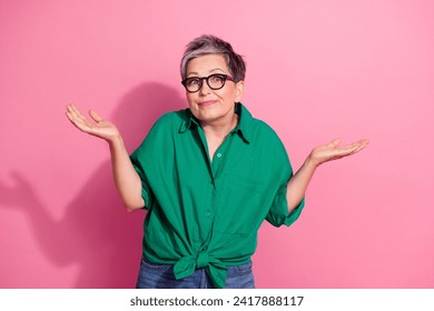 Photo portrait of attractive pensioner woman shrug shoulders dont know dressed stylish green clothes isolated on pink color background