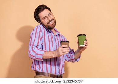 Photo portrait of attractive young man talk phone hold coffee paper cups dressed striped formalwear isolated on beige color background - Powered by Shutterstock