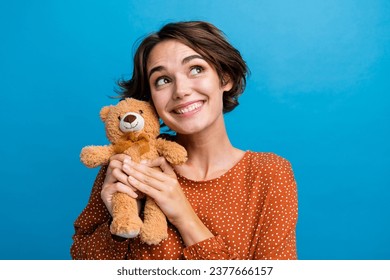 Photo portrait of attractive young woman hold teddy bear look empty space wear trendy brown clothes isolated on blue color background
