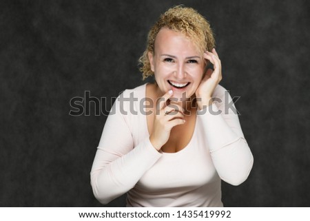 Photo portrait of a beautiful girl blonde woman with short curly hair on a dark gray background talking and showing a lot of emotions. Shows hands. Beauty. Made in a studio.