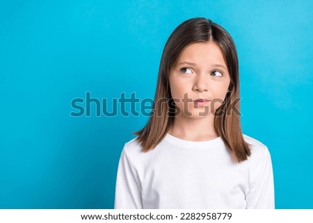 Photo portrait of charming schoolgirl look skeptical doubtful empty space dressed stylish white clothes isolated on blue color background