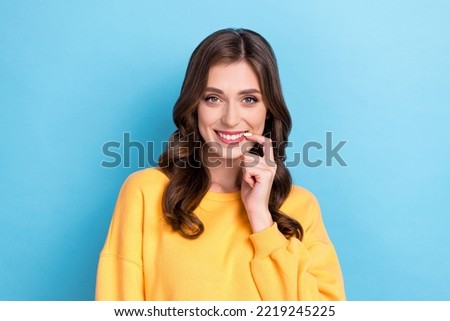 Photo portrait of charming young girl bite nail smiling flirty interested look wear trendy yellow clothes isolated on blue color background