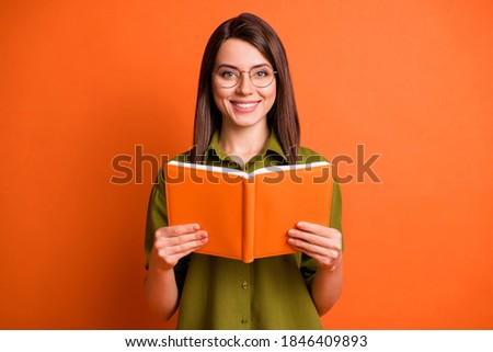 Photo portrait of cheerful female student wearing glasses keeping book smiling isolated on vibrant orange color background