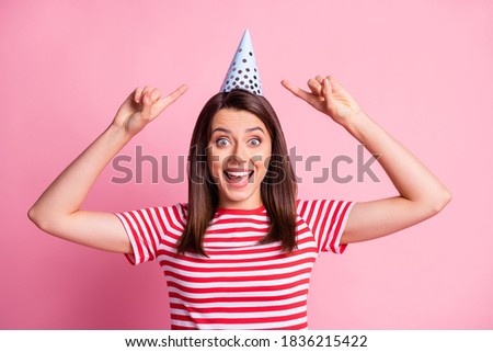 Photo portrait of cheerful funny girl pointing with fingers on birthday cap smiling isolated on pastel pink color background