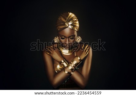 Photo Portrait closeup fantasy african woman face in gold paint. Golden shiny skin. Fashion model girl goddess hand fingers posing. Arab turban head, jewellery bracelets. metallic makeup. black studio