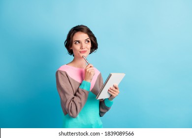 Photo portrait of curious girl thinking about idea keeping pen notebook looking at copyspace isolated on bright color blue background