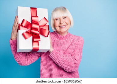 Photo Portrait Of Curious Old Lady Holding Present Box Near Ear Shaking Guessing What's Inside Isolated On Pastel Blue Colored Background