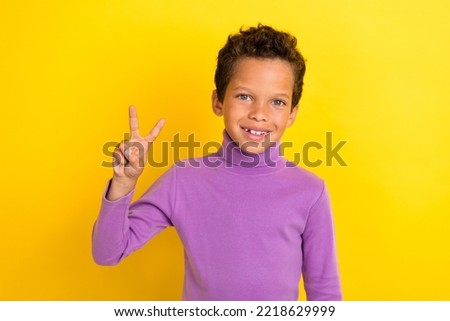Photo portrait of cute little boy showing v-sign optimistic beaming smile wear trendy violet garment isolated on yellow color background
