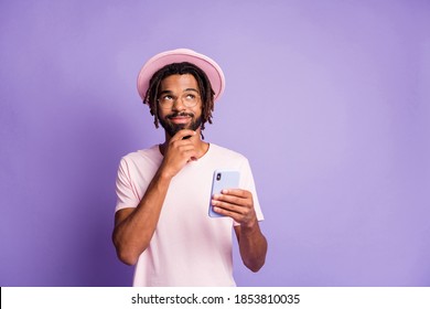 Photo portrait of dreamy man in stylish pink hat headwear holding phone in one hand touching beard isolated on vivid violet colored background - Powered by Shutterstock