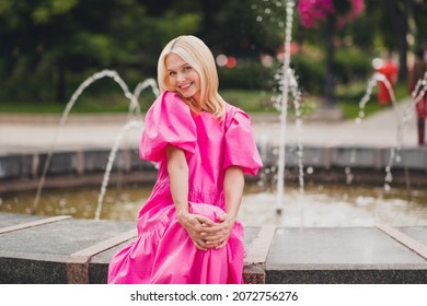 Photo portrait elder woman with blonde hair browsing wearing pink dress sitting on fountain in city having good mood