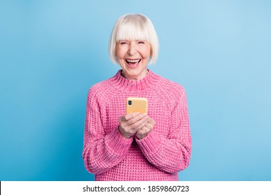 Photo Portrait Of Excited Old Woman With Open Mouth Holding Phone In Two Hands Isolated On Pastel Blue Colored Background