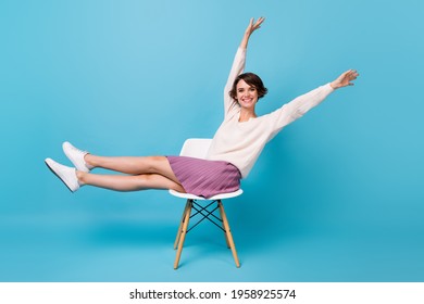 Photo portrait full body side profile view of excited girl lifting legs arms up sitting on chair isolated on pastel blue colored background