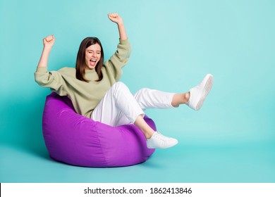 Photo portrait full body view of crazy woman screaming raising two legs and arms fists up sitting in purple bean bag chair isolated on vivid cyan colored background - Shutterstock ID 1862413846