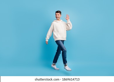 Photo Portrait Full Body View Of Walking Man Waving Hand Wearing Woolen Hoodie Isolated On Pastel Blue Colored Background