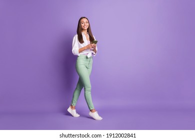 Photo portrait full body view of woman walking holding phone in two hands isolated on vivid purple colored background