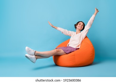 Photo portrait full body view of girl waking up stretching sitting in orange beanbag chair isolated on pastel blue colored background - Shutterstock ID 1923600386