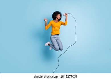 Photo portrait full length of singing woman holding mic in one hand jumping up isolated on pastel blue colored background