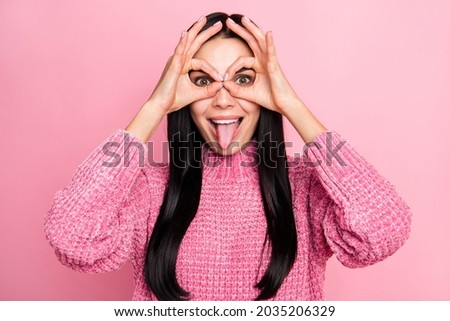 Photo portrait of funny girl making glasses with fingers showing tongue isolated on pastel pink colored background