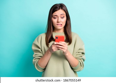 Photo portrait of girl biting lower lip holding phone in two hands isolated on vivid turquoise colored background