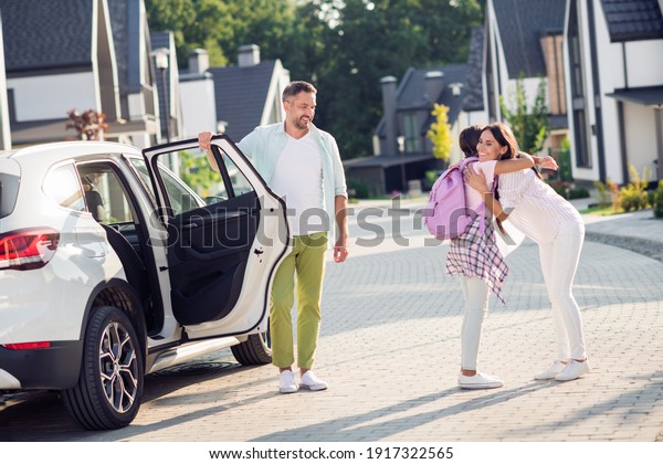 Photo portrait of girl hugging mother\
coming back from school exiting white car\
outdoors