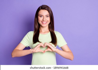 Photo portrait of girl wearing green t-shirt showing heart with hands smiling isolated on vibrant purple color background