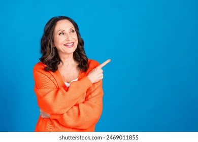 Photo portrait of gorgeous senior woman point look empty space wear trendy orange outfit hairdo isolated on blue color background - Powered by Shutterstock