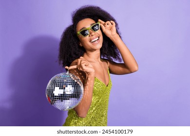 Photo portrait of gorgeous young girl sunglass hold discoball wear trendy green sequins outfit isolated on purple color background - Powered by Shutterstock