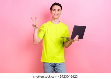 Photo portrait of handsome teen male show v-sign hold netbook wear trendy yellow garment isolated on pink color background