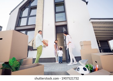 Photo Portrait Of Happy Family Of Four Moving To New Home Carrying Boxes Going Inside Modern House Outdoors In Summer On Street