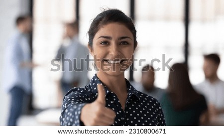 Photo portrait of happy Indian female business leader gesturing like, showing thumb up. Team working in background. Satisfied client woman gives approval positive feedback, recommends company service
