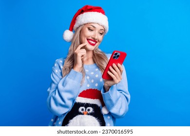 Photo portrait of lovely blonde young lady hold telephone interested wear penguin sweater x-mas hat isolated on blue color background - Powered by Shutterstock