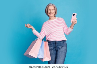 Photo portrait of lovely pensioner lady hold device shopping bags dressed stylish striped garment isolated on blue color background - Powered by Shutterstock